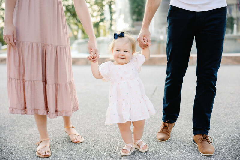 little girl standing between parents holding their hands