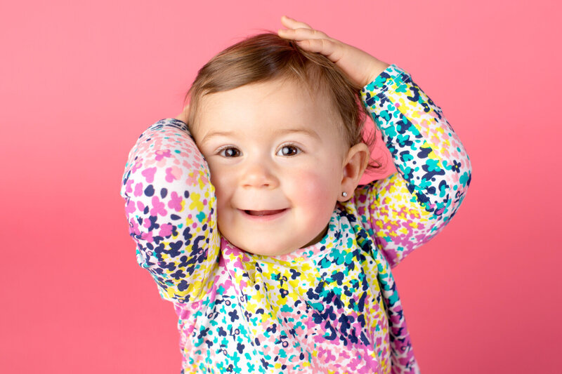 Closeup of a baby girl in a colorful shirt on a pink background