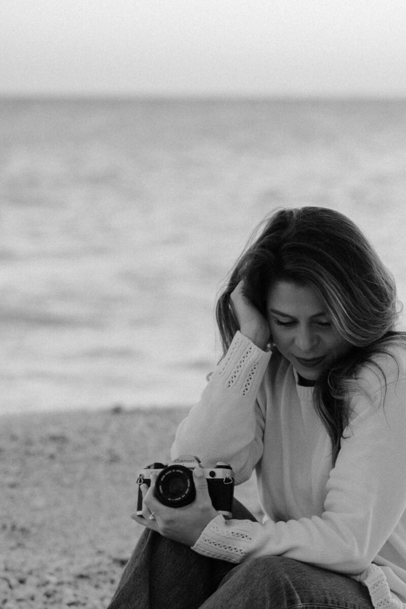 woman sitting on the beach while holding a camera with her head in her hand