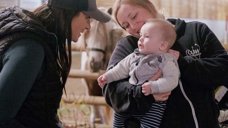 A mentor at Spirit’s Respite Ranch talking gently with a baby, nurturing connection and a sense of calm in a serene natural setting.