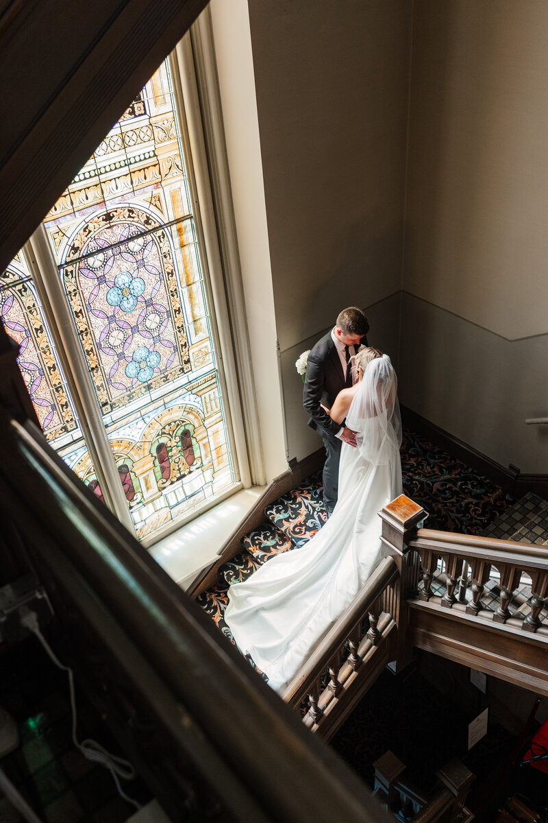 Wisconsin bride and groom tenderly embracing in a church stairwell near a stained glass window