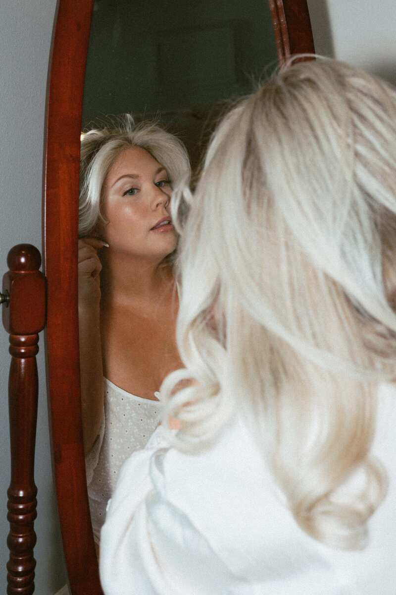 A bride looks at her reflection in a mirror representing bridal makeup by Looks with Libby.