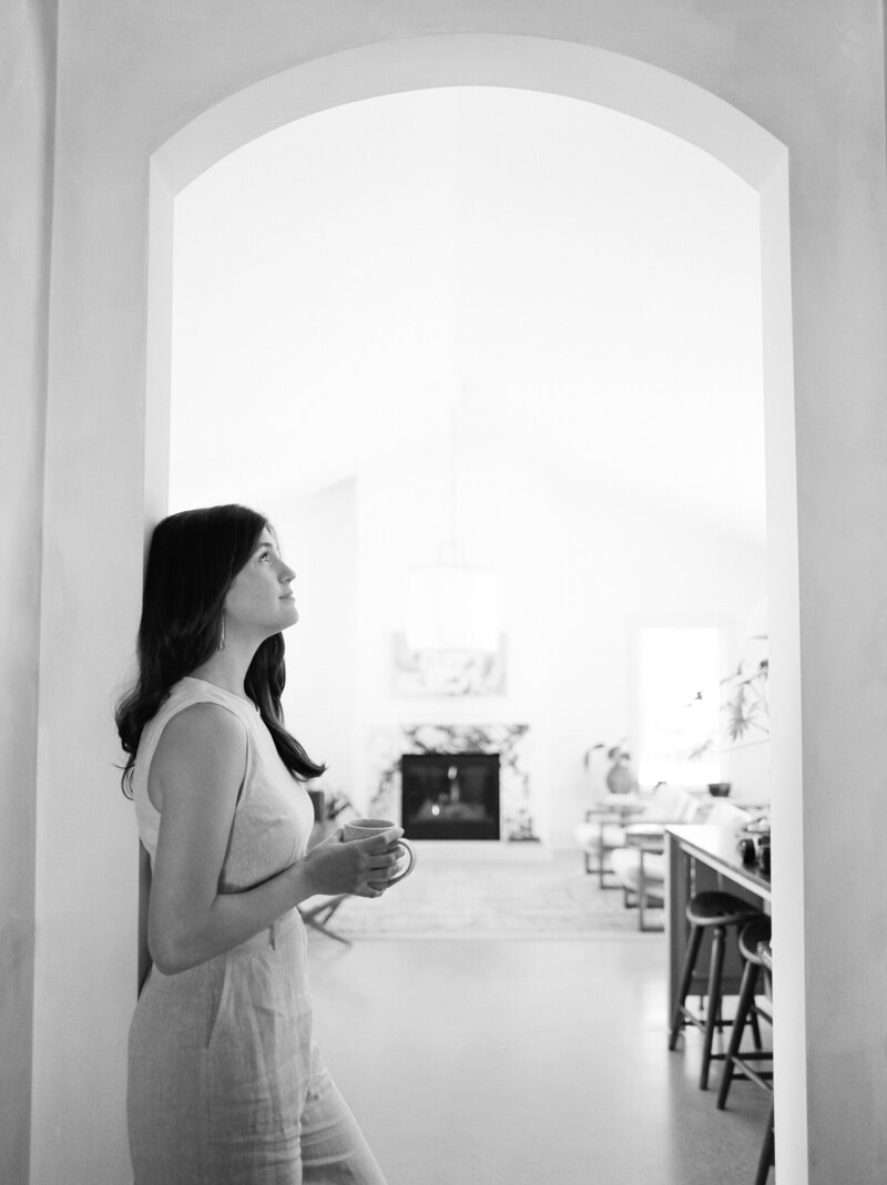 relaxed, natural designer in beige linen jumpsuit, under arch with coffee at Fernhaus, Michigan film brand photoshoot