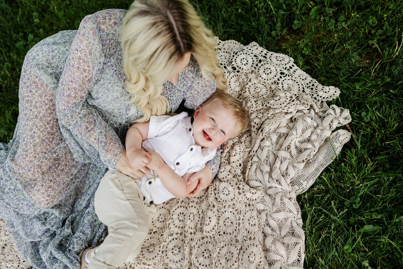Mother tickling son while he looks up at the camera laughing taken by Jennifer Mosier Photography. 