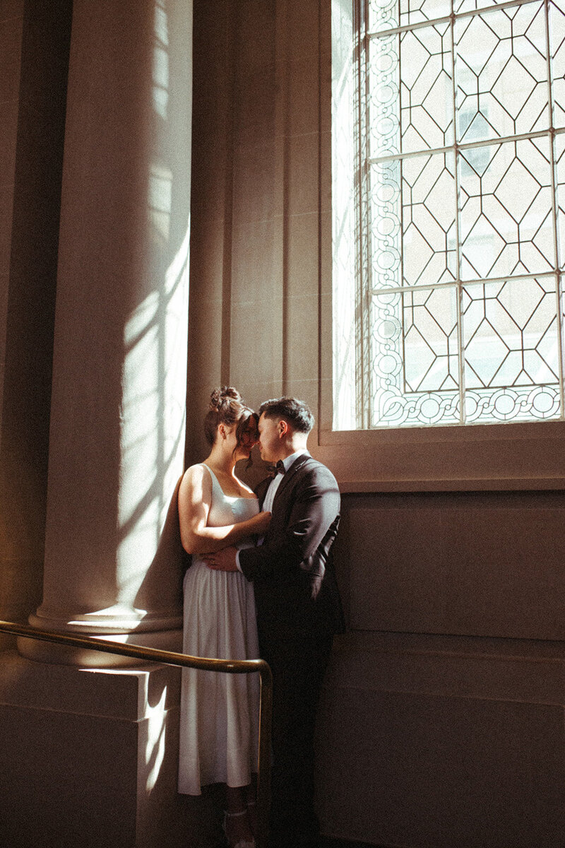 A bride and groom cuddle in a corner of San Francisco City Hall