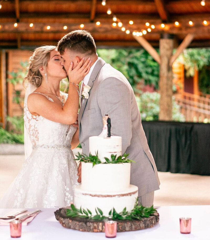 A newlywed couple sharing a kiss by their wedding cake