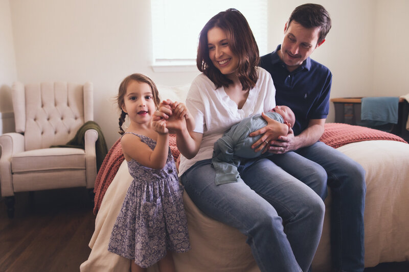 Family photographer capturing a mom, dad, and two children playing in bed.