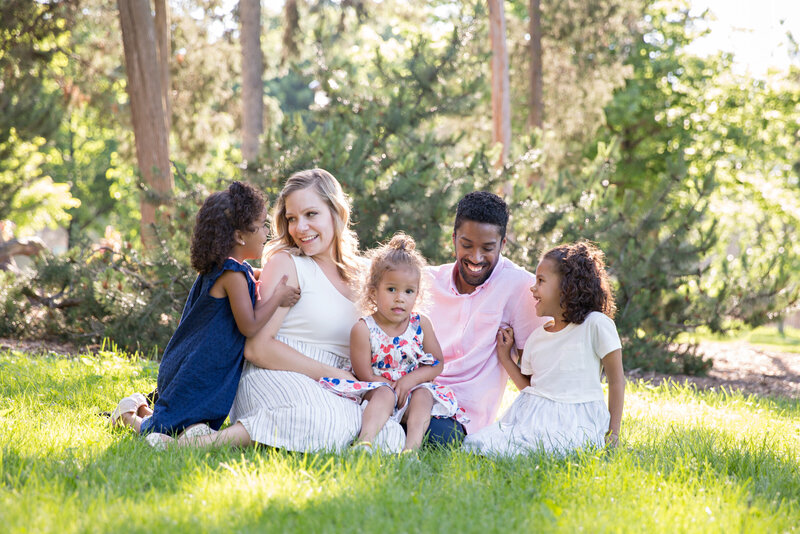 biracial family sitting on the grass laughing
