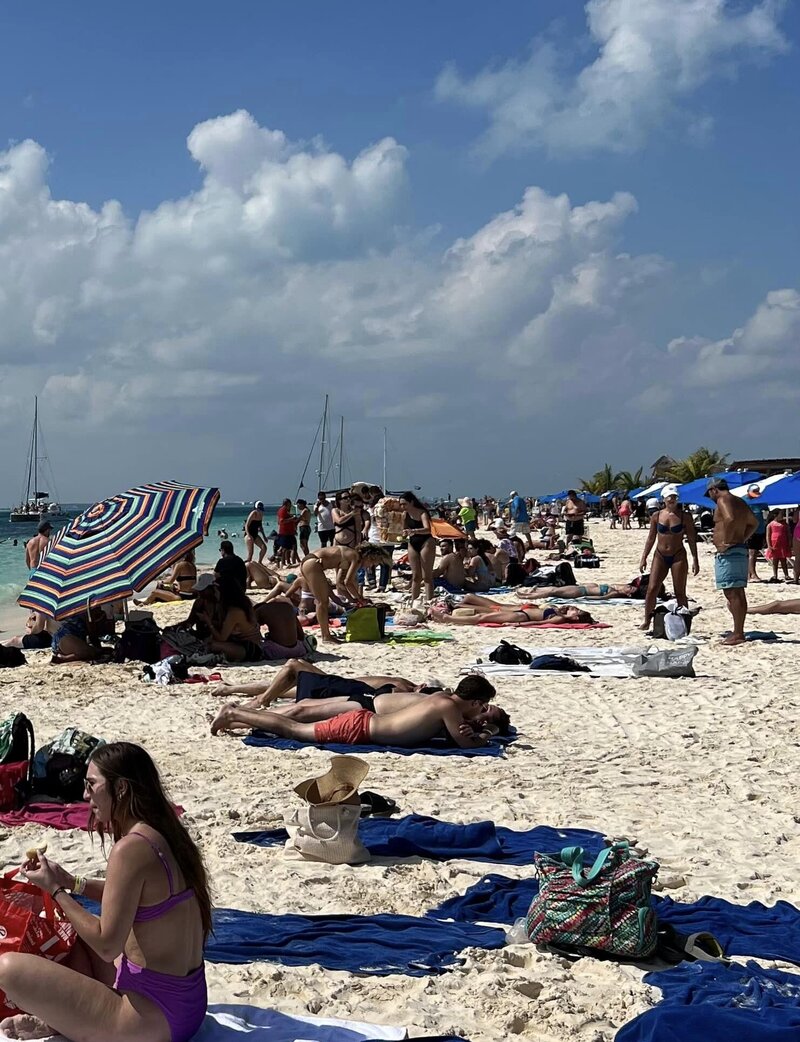 People lay on crowded beach with blue towels and striped umbrellas
