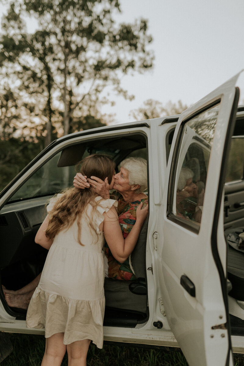 A candid photograph of a granmother kissing her daughter on the cheek from the front seat of a ute during a multi-generational photoshoot in grafton