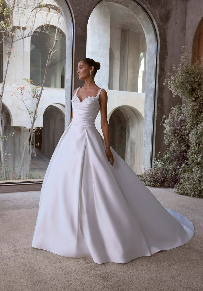 Bride posing indoors in a fitted ball gown with lace detailing on the bodice