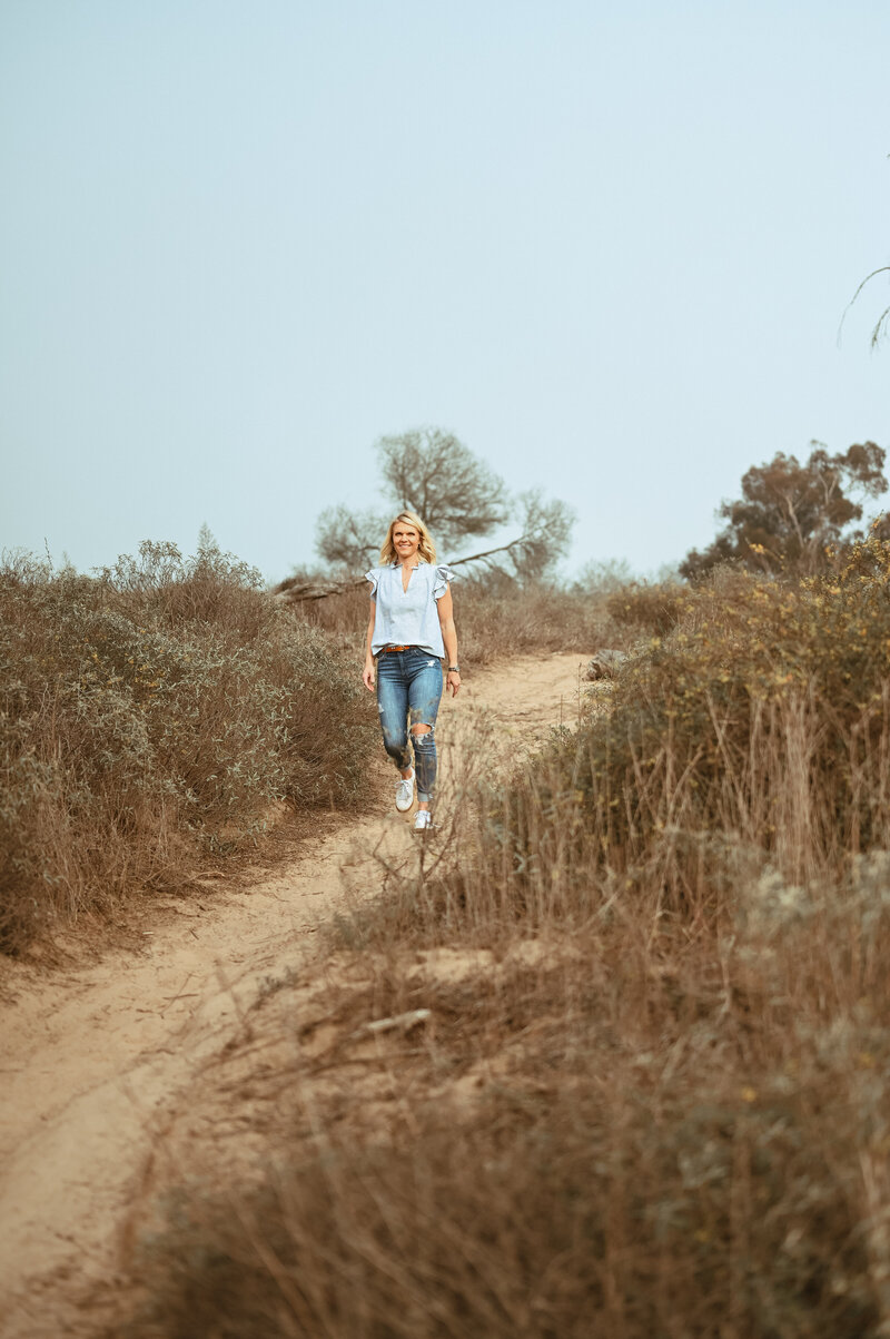 Emily Collins walking a dirt path in nature, representing her blog about motherhood and business.