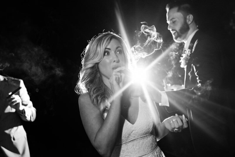 Bride and groom enjoying cigars in the dark illuminated by a bright light