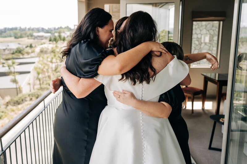 bride and bridesmaids in black ruby dresses group hug on balcony at fable terrace downs