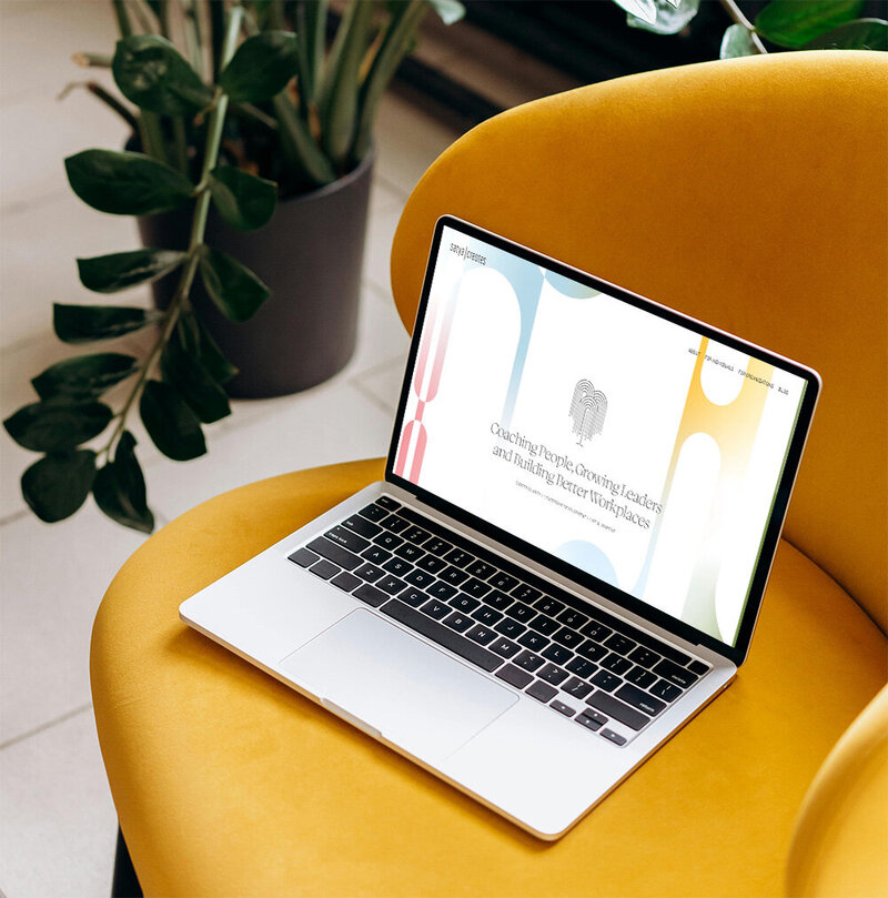 Silver laptop on orange chair next to a plant in a black pot