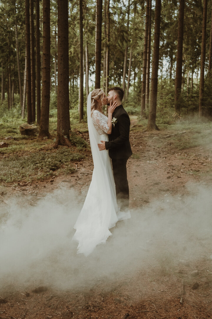Een bruidspaar in de Belgische Ardennen dat elkaar kust met een rookbom