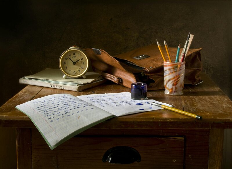 Image of a desk with a journal, pencils, a mini clock and messenger bag.