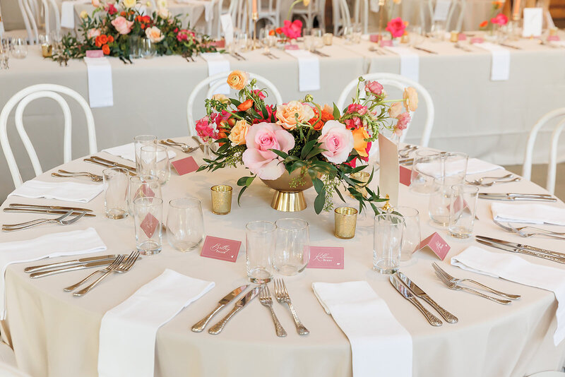 Chic spring wedding reception setup with gold and blush accents and a centerpiece bursting with pink, coral, and orange florals.