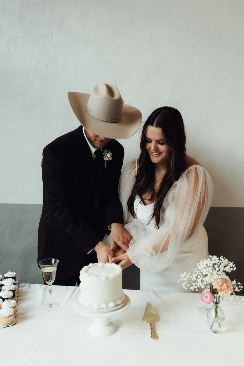Country Kansas Wedding| Bride and groom cutting wedding cake photo| Long sleeve wedding dress| cowboy hat on the groom.