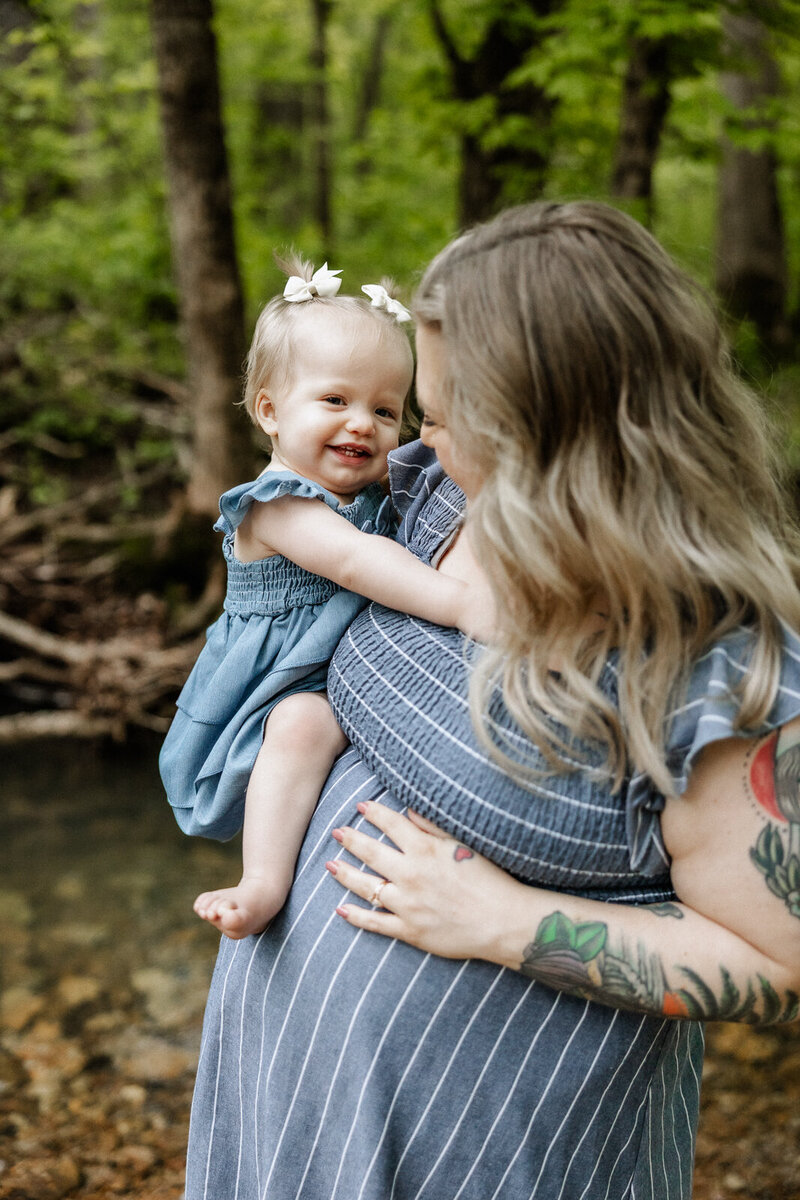 Candid maternity portrait of mom-to-be laughing with  her toddler while holding her. 