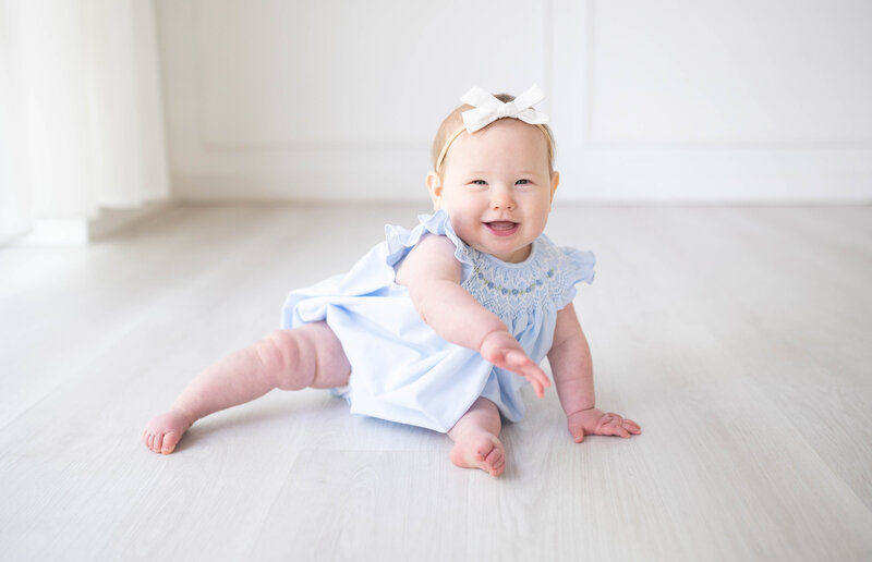 A one-year-old baby at the Lumen Room wearing a smocked outfit smiles during her one-year photos.
