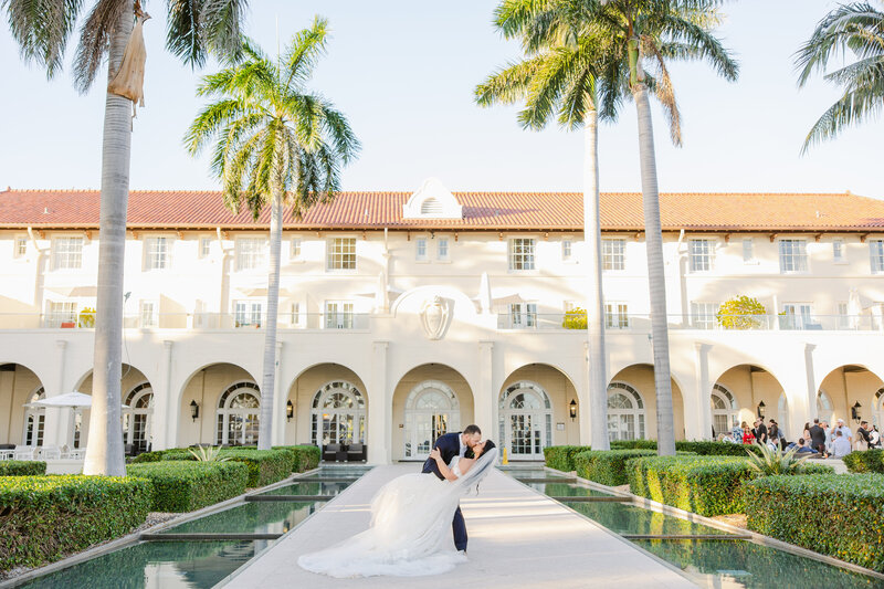 Bride and groom kiss in front of a luxury vacation resort.