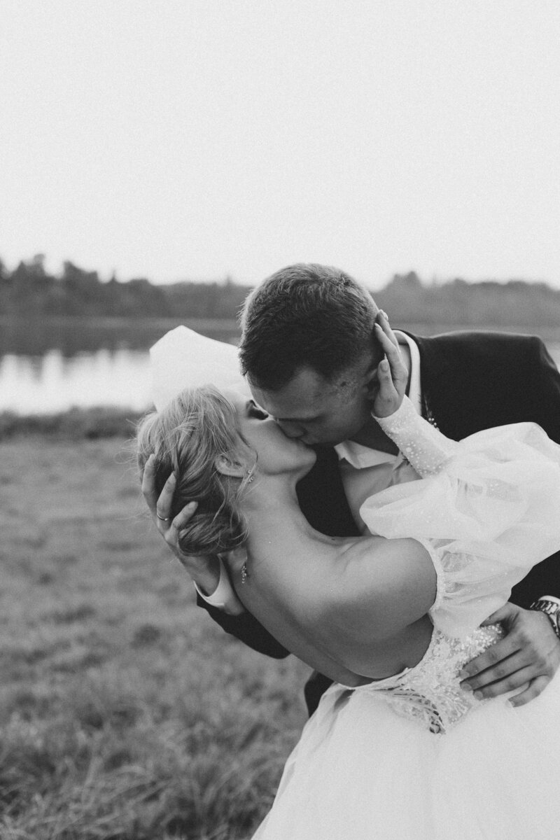 Timeless black and white photograph capturing the bride and groom sharing a passionate kiss while dipping, exuding romance and joy on their wedding day.