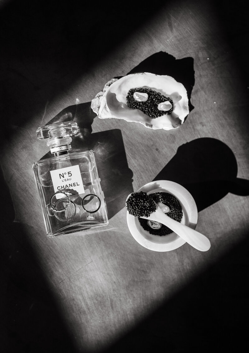 Black and white flatlay with Chanel No. 5 perfume, wedding rings, and caviar in dramatic lighting