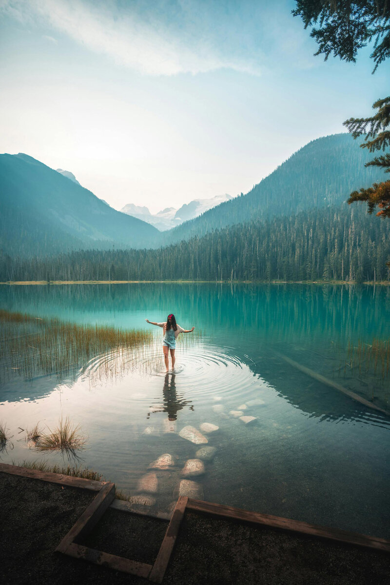 Woman playfully stepping into a lake in front of mountains