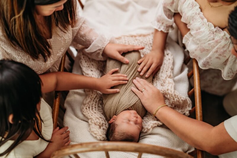 newborn boy sleeping in vintage crib with his parents and sisters hands resting on him