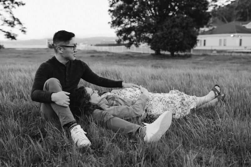 black and white maternity photo of mom laying on dad's lap in a field