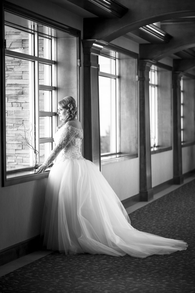 Black and white photo of a bride looking out the window before her wedding.