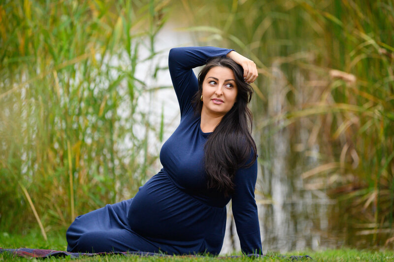 Pregnant woman sitting on the ground wearing a blue maternity dress with her arm draped over her head for her Burlington, Ontario Maternity Photography Session
