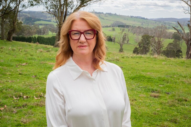 Suzanne Harrison wearing a white shirt and red glasses in a green field 