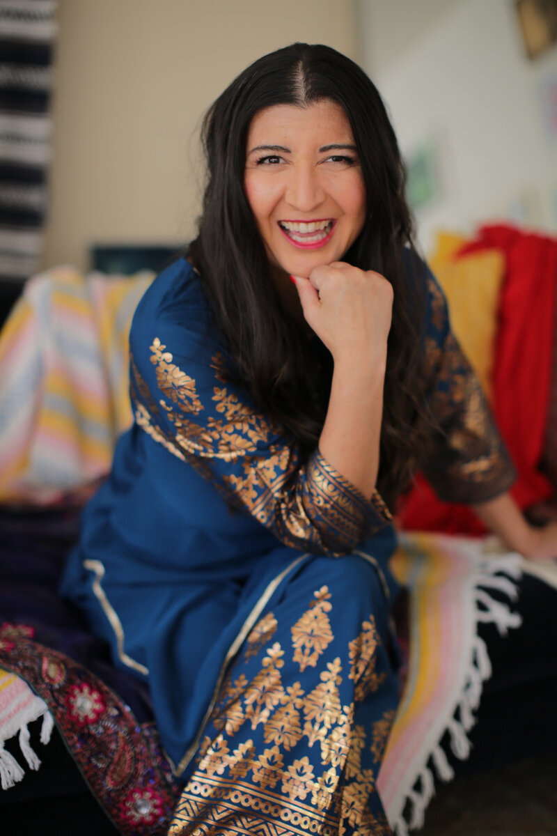 Women in golden light, wearing dark rimmed glasses and striped shirt, smiling down at her hands as she rolls out clay