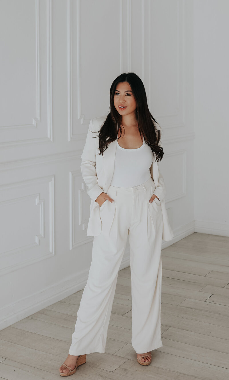 entrepreneur woman standing in white suit and smiling with hands in her pockets.
