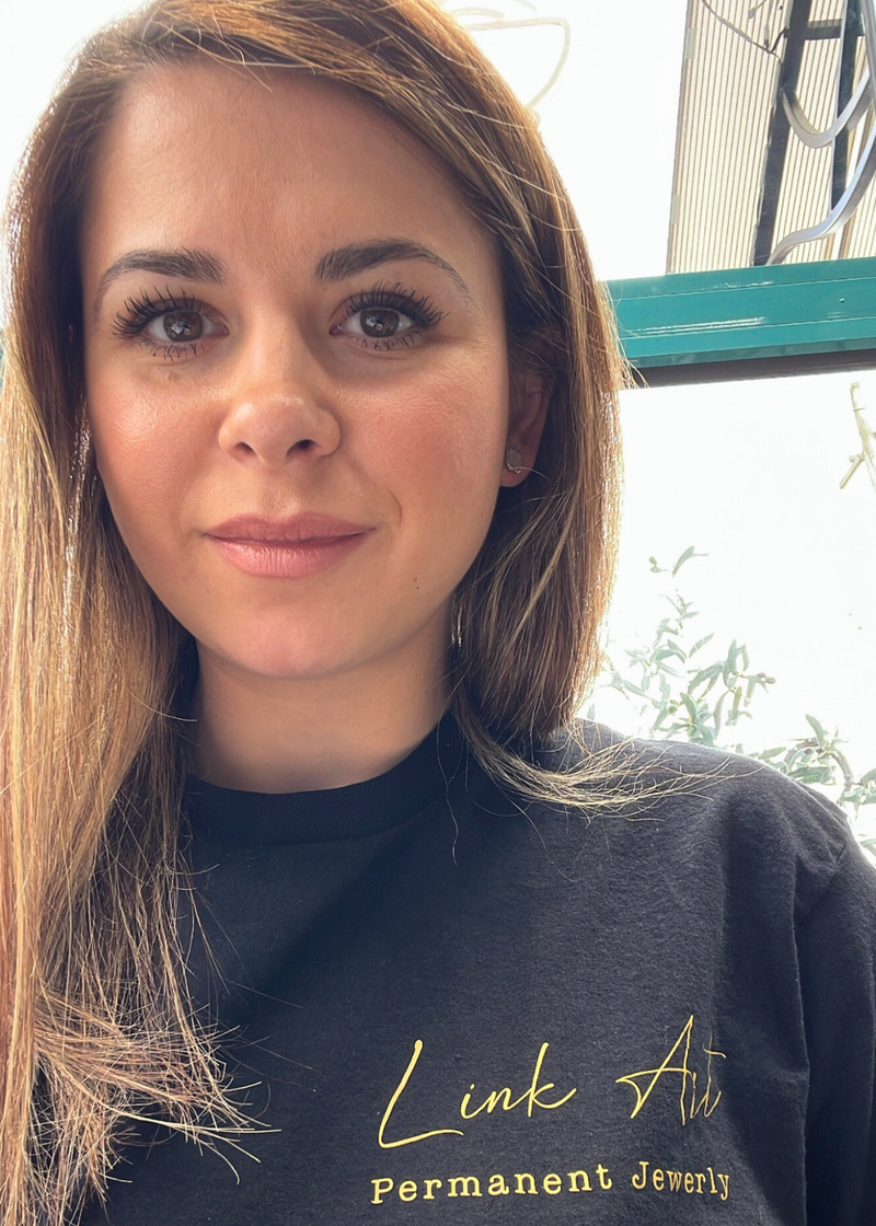 Portrait of Denisa, owner of Link Art Permanent Jewelry, smiling in branded t-shirt.