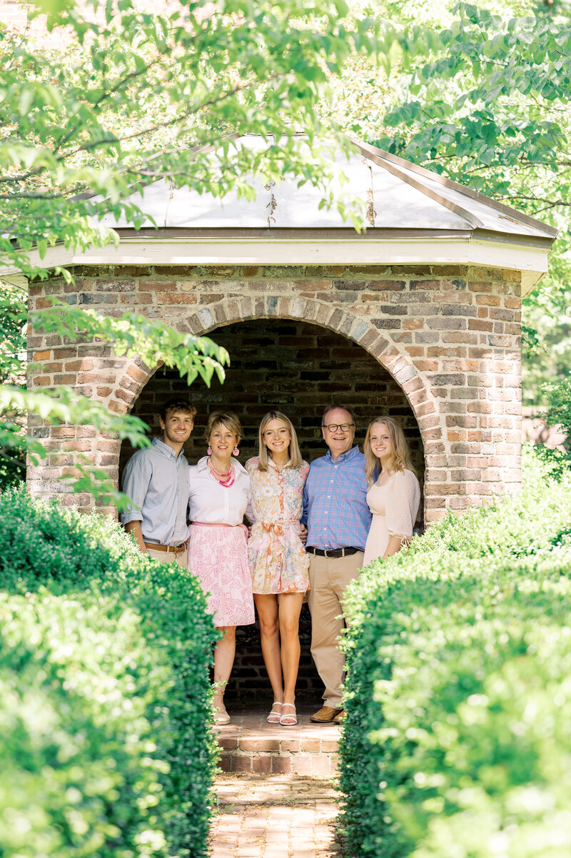 Family of four posing in front of green grass and trees