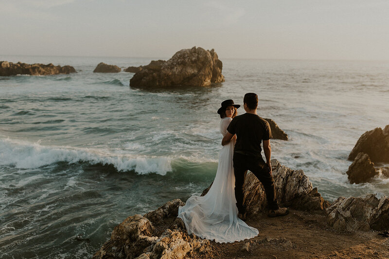 bride and groom on a rock by the ocean