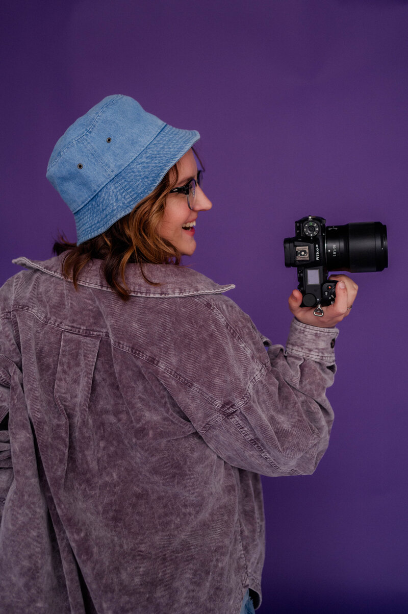 Rachel Hahn, owner of Rachel B Photographer, smiles of into the distance with her camera in hand.