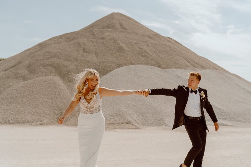 bride and groom holding hands and running through sand dunes