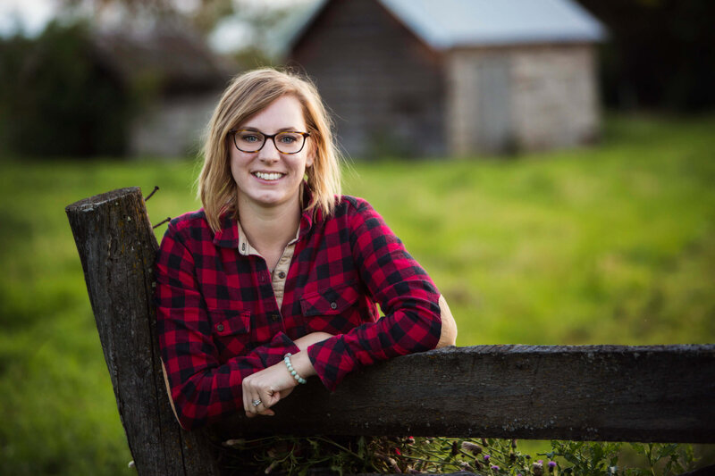 girl in red plaid leans on old fence while smiling