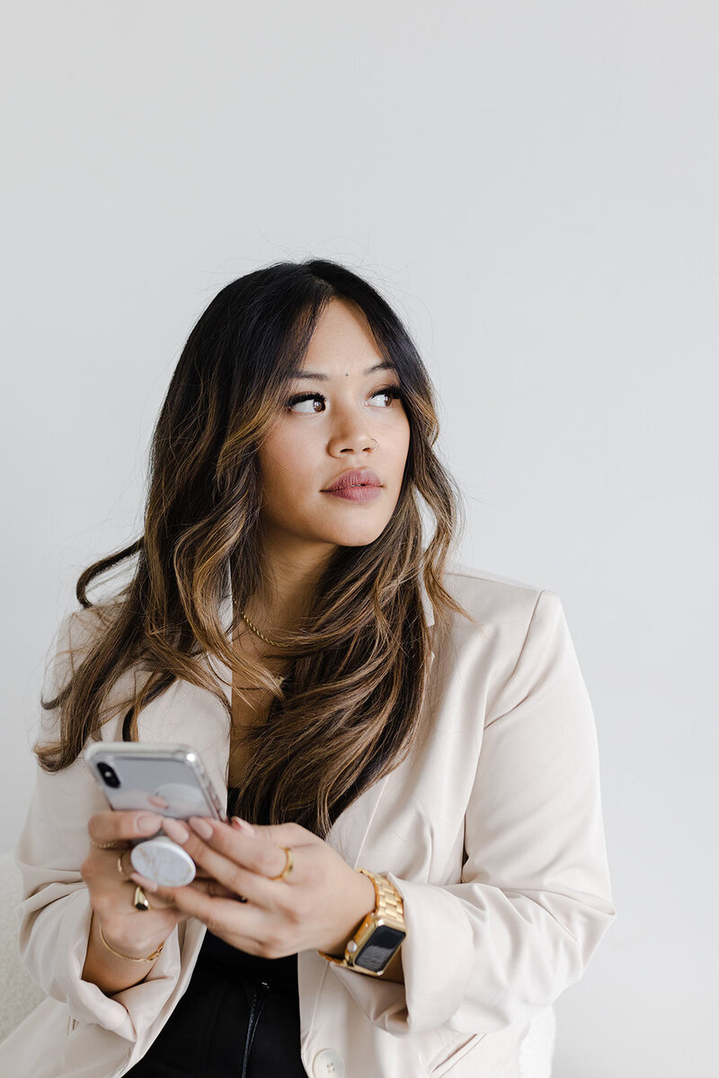 female entrepreneur in a cream blazer stares off into the distance with her mobile phone in her hand