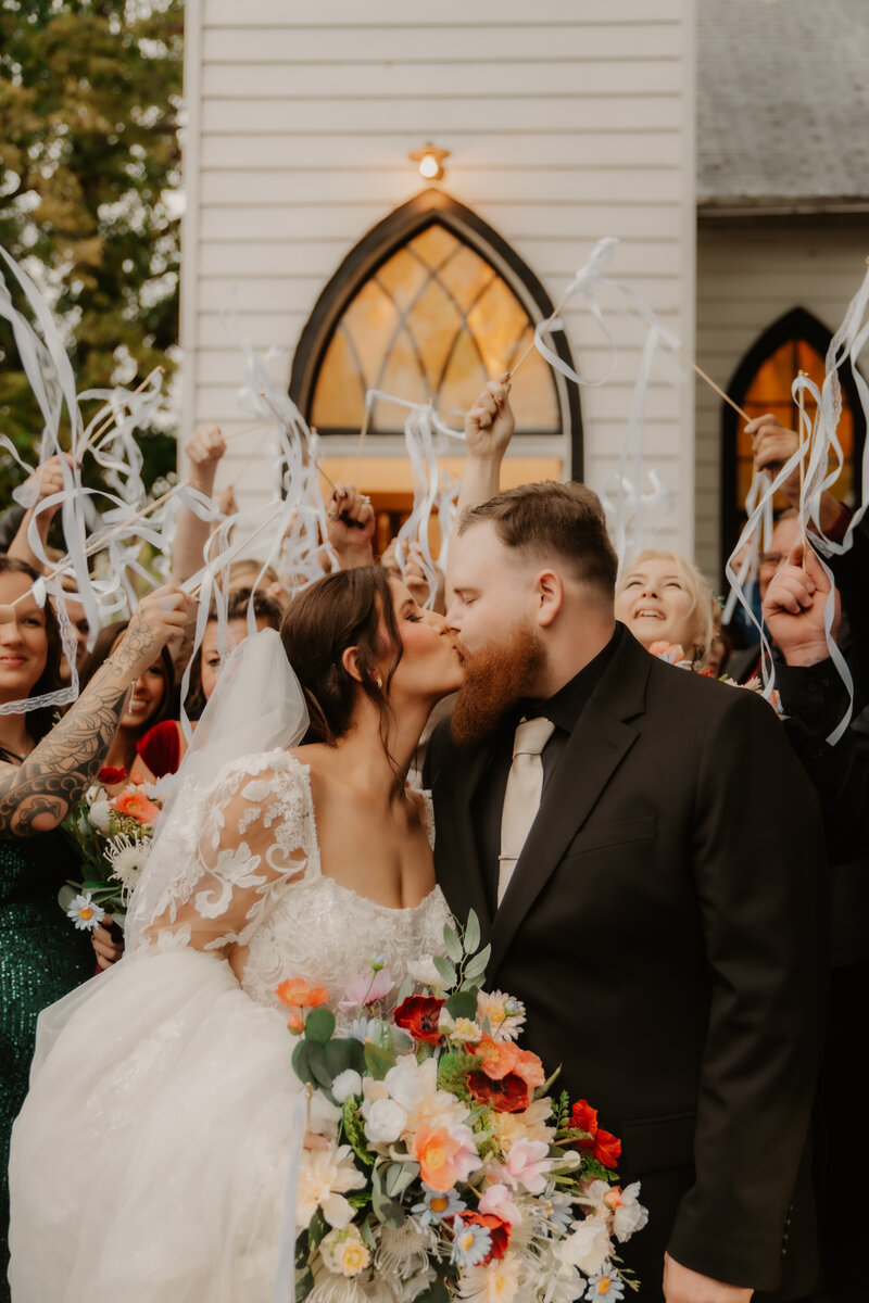 Bride and groom leaning against a wall in black and white with groom suit and bride in wedding dress with flower bouquet