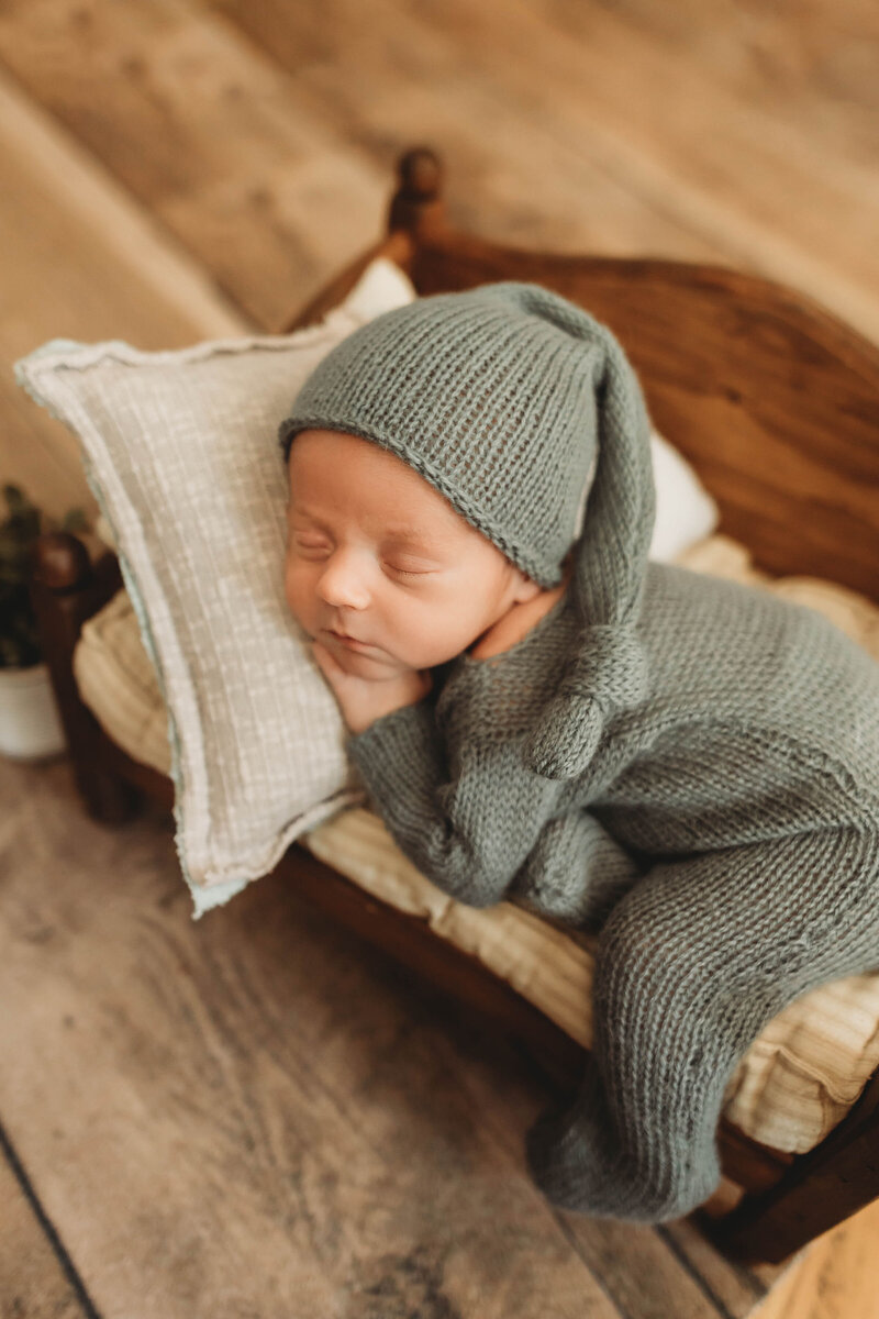 newborn baby boy in a knitted outfit sleeping on a tiny bed