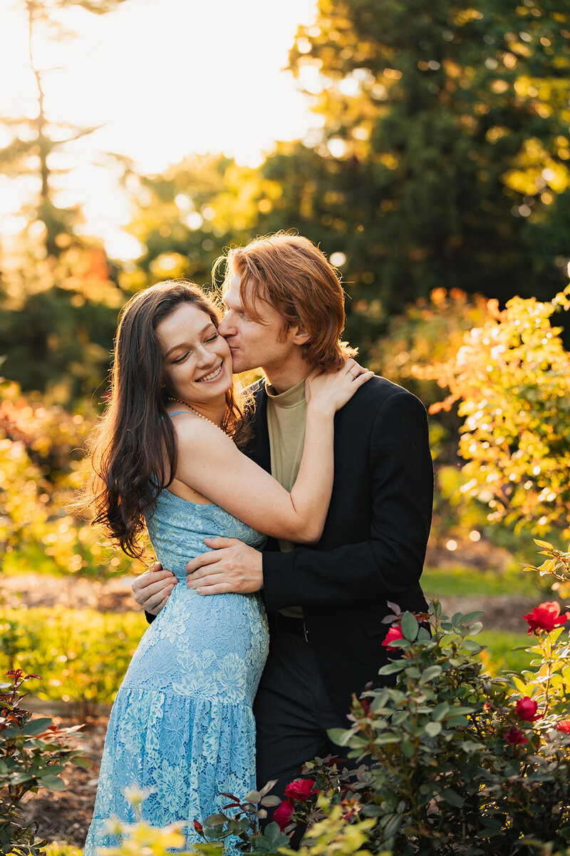 a man kissing a woman on the cheek during a couple photoshoot in a rose garden during golden hour  in montclair new jersey