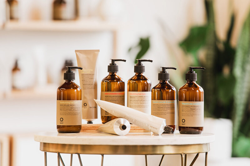 A collection of OWay hair products displayed on a round table representing non-toxic hair products used at the The Collective Beauty and Wellness.