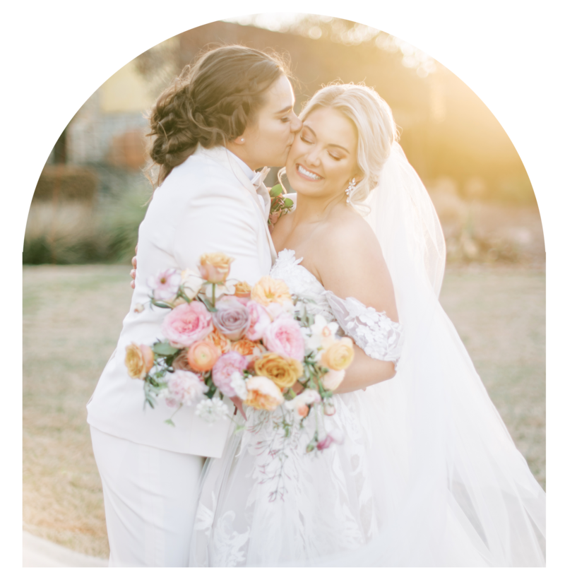Couple nuzzling noses on wedding day with colorful bouquet.