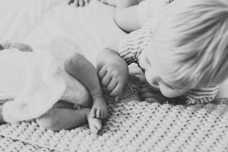 A serene newborn baby is sleeping, wrapped snugly in a soft, neutral-toned fabric. The baby has closed eyes and a calm expression, lying against a gentle, textured backdrop that enhances the cozy atmosphere.
