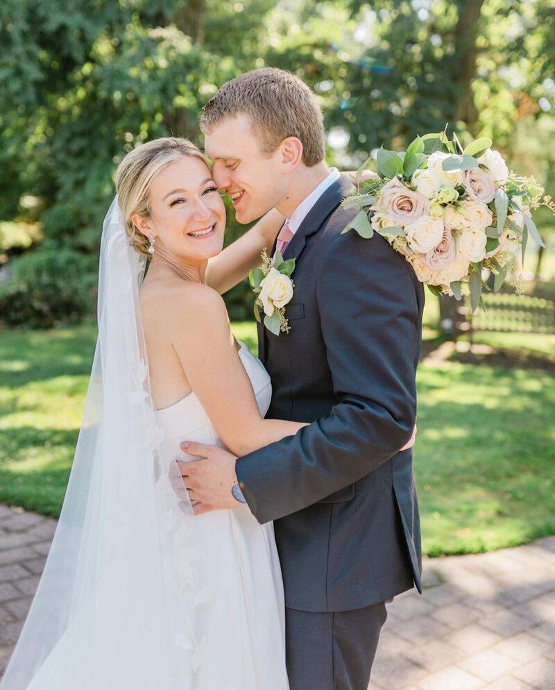 Bride happily hugging the groom while holding her floral bouquet and groom about to kiss her bride's cheeks